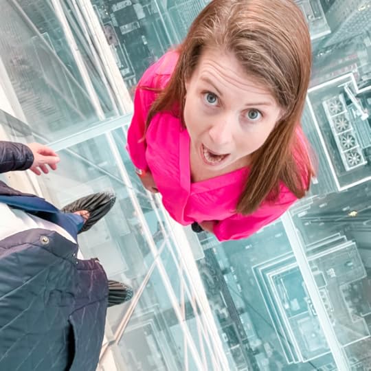 Amy Julia stands on the glass-encased floor of One Vanderbilt. Her mouth and eyes are wide open and she looks up at a camera high above her. 