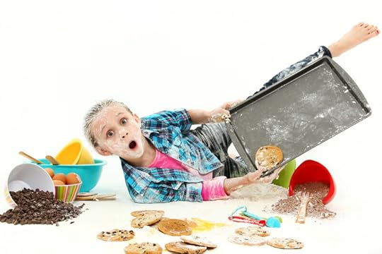 A silly photo of a boy who looks like he's fallen on the floor while baking. He is covered in flour and surrounded by spilled ingredients for chocolate chip cookies as well as actual finished cookies. Dyspraxia can cause difficulty with motor skills, coordination, and balance.