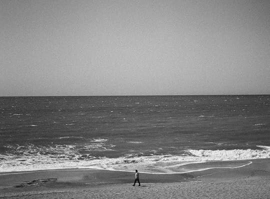 Black and white photo of a man walking alone on a beach.