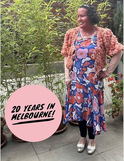 Image: a woman with a red face, short dark curly hair, standing on a balcony with trees near her. She's wearing a blue, peach and pink floral dress, pink and silver shoes and a 3D rose jacket over her dress. She's standing side on, smiling. A peach circle with