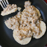 black dish of split biscuits with sausage gravy.