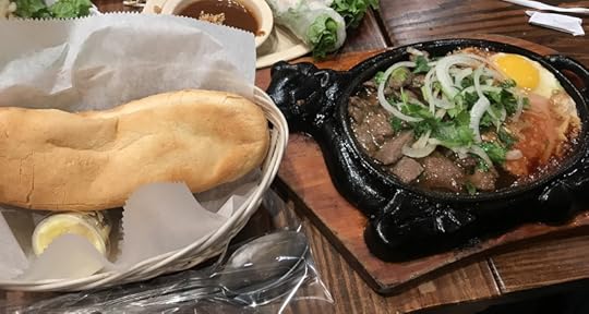 Fresh baguette next to cow-shaped sizzling platter with steak and eggs, topped with onions and cilantro