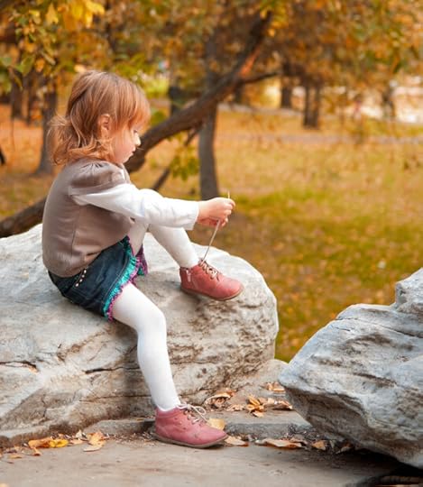 Photo of a young girls outside during fall sitting on a rock and trying to tie her shoes. Difficulty learning to tie shoes when young can be one of the effects of dyscalculia because it involves memorizing a sequence of steps.
