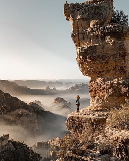 Tourist standing under rough cliff in mountains by Jarod Lovekamp