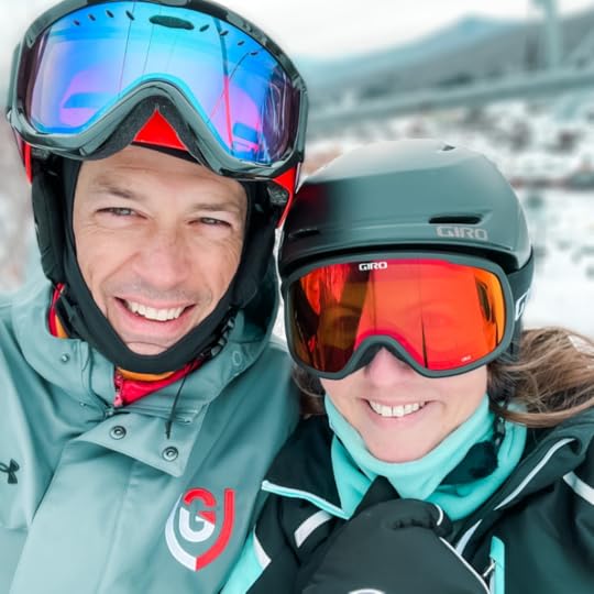 Peter and Amy Julia smile for a selfie. They are wearing ski goggles and there is a snowy slope behind them