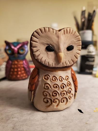 A small barn owl sculpture made of polymer clay. It's painted with various shades of creams, browns, yellows, and oranges.