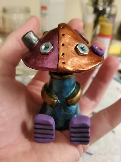 A mushroom robot painted in metalic colors of copper, berry, teal, bronze, and lavender. It is sitting in a hand to show its small size, about 3 inches tall.