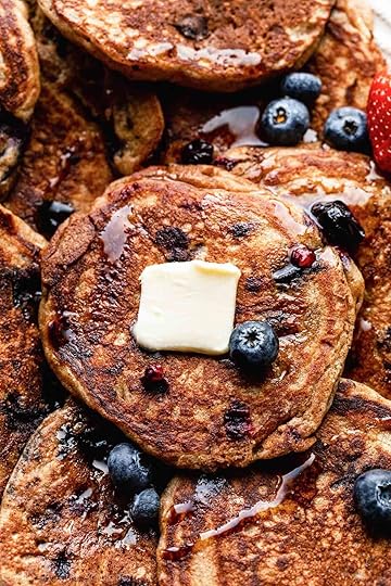 close-up of whole wheat blueberry pancakes with maple syrup, butter, and fresh blueberries on top.