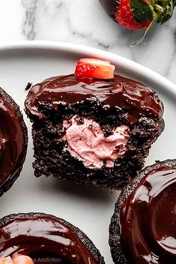 close-up of chocolate covered strawberry cupcake filled with strawberry buttercream and sliced open.