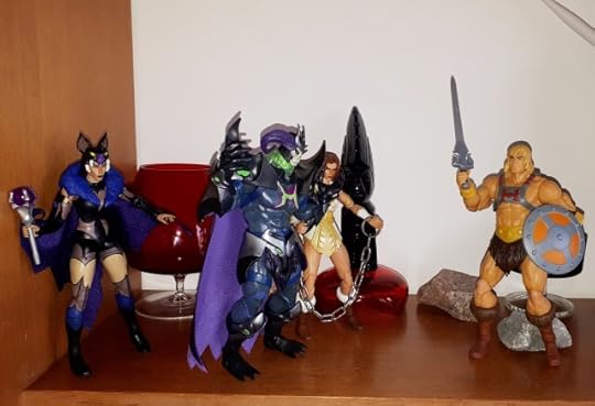 Skelegod threatens the chained up Teela in front of He-Man, while Evil-Lyn looks on.