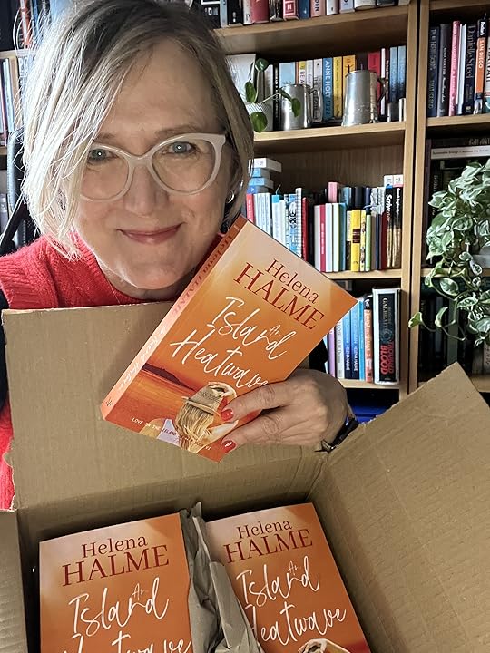 An image of Helena Halme smiling as she holds a box of paperback copies of AN ISLAND HEATWAVE.