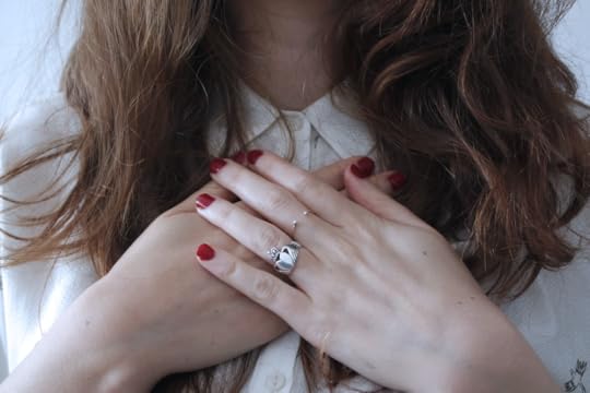 A woman's hands are clasped just below her neck, as if taken aback.