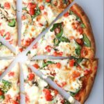 greek pizza baked and sliced on white cutting board.