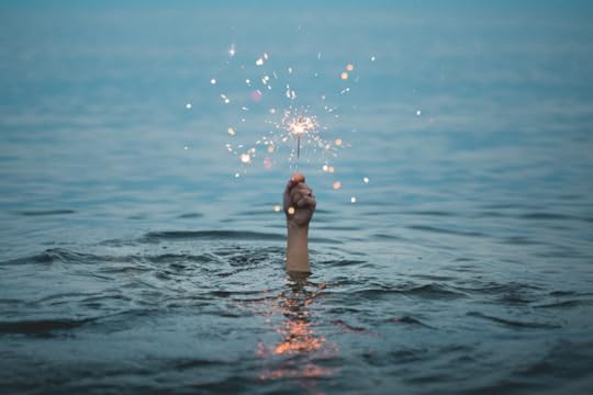 From underwater a lone hand emerges, holding a sparkler.