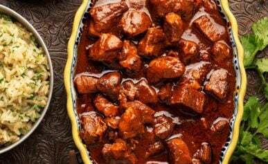 A bowl of asado de puerco with beans and rice alongside.