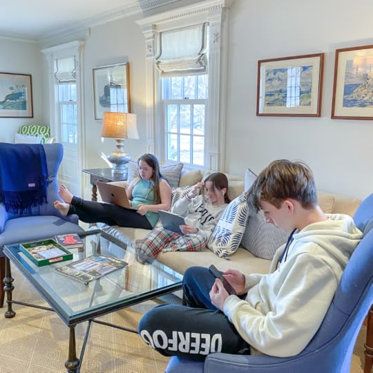3 kids sit in a living room looking down at mobile devices