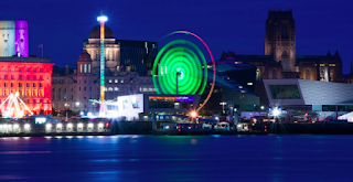 The Pier Head in Liverpool, by night. Buildings on the waterfront, illuminated in bright colours.