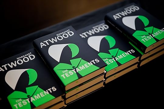 Copies of Testaments by Margaret Atwood laid out on a table, black and green cover showing a woman in a hood