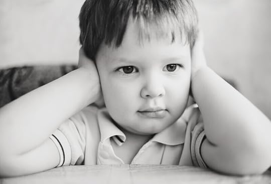 black and white photo of a young boy with his hands over his ears. Children with auditory dyslexia may cover their ears.