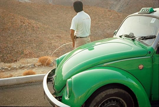 A color photograph of a man standing beside a green Volkswagen taxi