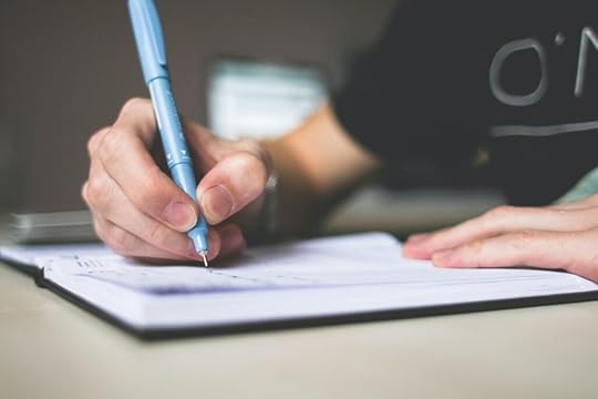A person holding blue ballpoint pen writing in notebook.