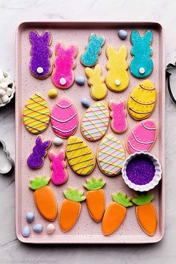 decorated Easter cookies on pink baking sheet including bunnies with marshmallow tails, Easter eggs, and carrots with orange and green icing.