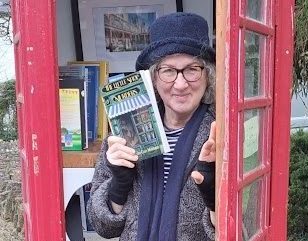 Debbie with a paperback copy of Little Shop of Murders in a red phone box community library