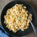 black dish with Mac and cheese topped with green onion, next to blue cloth.