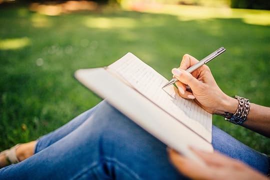 A person writing on a notebook outside on the grass.