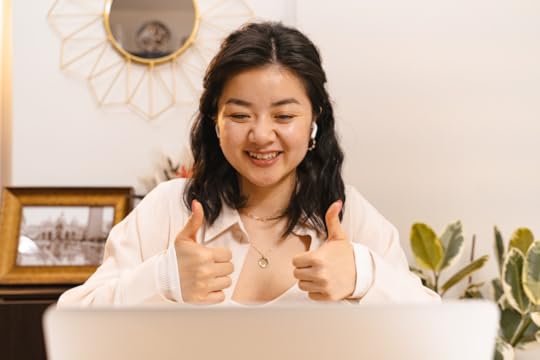 Image: Sitting in front of a laptop computer, a smiling woman wearing earbuds gives two thumbs up to the computer screen.