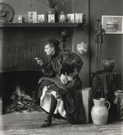 Frances Benjamin Johnston, full-length portrait, seated in front of fireplace, facing left, holding cigarette in one hand and a beer stein in the other, in her Washington, D.C. studio