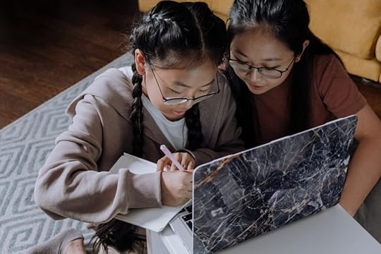 A girl writing in her notebook with another girl watching beside her.