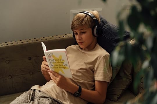 A teenage boy listening to music while reading a book. Reading can help you get some good ideas for novel writing.
