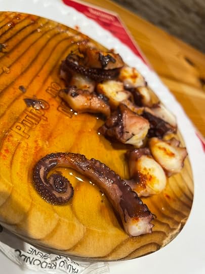 A curled octopus leg and several cut up pieces sit on a brown wooden plate