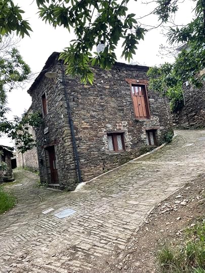 An old, dark stone house sits built into a steel hill, surrounded by uneven stone walkways