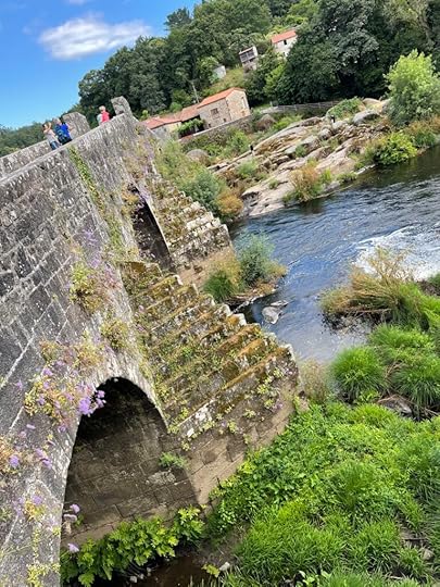 Pyramid-shaped roman pillars sit in the middle of a river, a large stone bridge resting on top of them