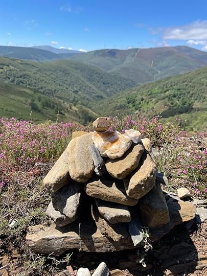 A stack of smooth rocks sits in the foreground, the background dark green rolling hills with a blue sky beyond