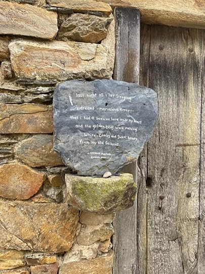 A dark slate stone hangs on a ran stone wall, with the words: