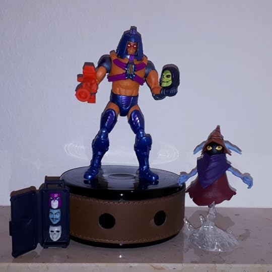 Man-e-Faces wears his human face and holds Skeletor's skull, while Orko looks on.
