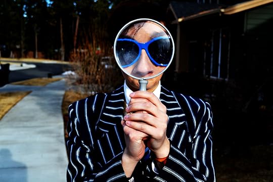 Photo of woman holding a magnifying glass up to her nose and eyes which appear through the glass to be larger than the rest of her body.