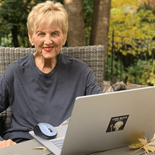 Image of Judith Humphrey seated outside at a table with her laptop open. She is smiling.