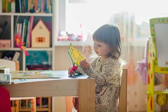 girl in white long sleeve dress sitting on brown wooden chair cutting paper -Autistic and ADHD Girls In Early Childhood