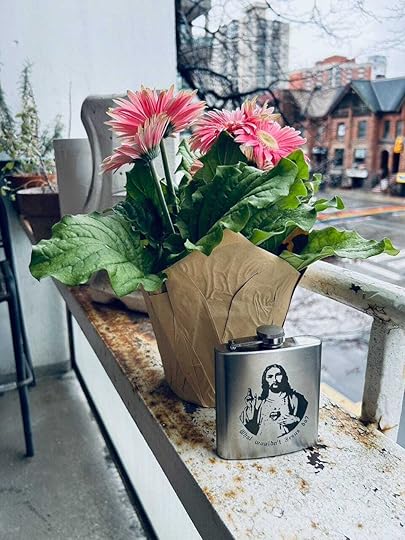 On a balcony, a potted plant of mums beside a flask with an image of Jesus on it and the words