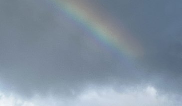 Image shows cloudy sky with a rainbow