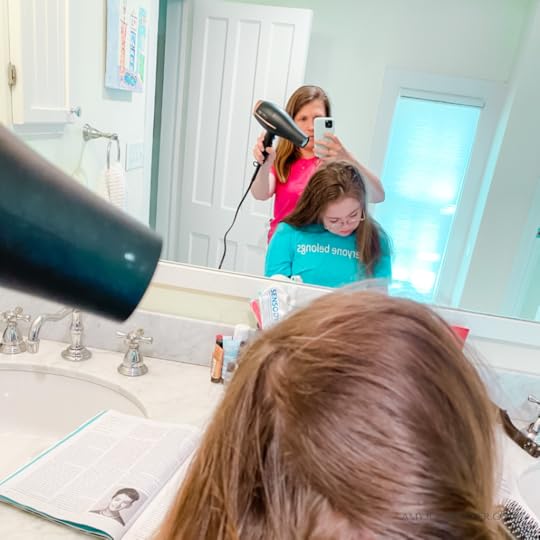 photo of Amy Julia taking a selfie in the mirror with her holding her cell phone and a hairdryer and Penny in front of her