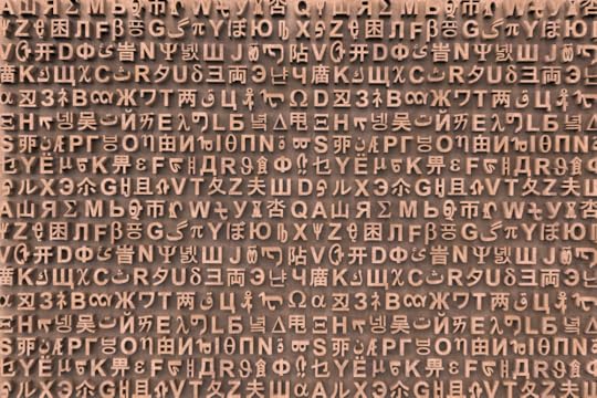 Image: an artwork comprised of many rows of three-dimensional characters from numerous languages mounted next to one another in random order on a backing board.