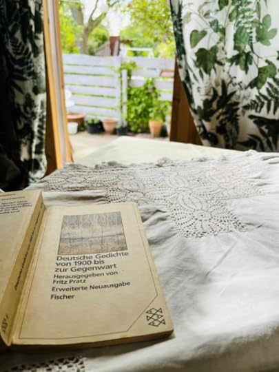 Einne aufgeschlagene Lyrikanthologie auf einem Tisch, im Hintergrund die geöffnete Laubentür, davor Grün