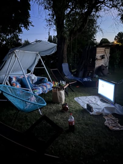 Eine Hollywoodschaukel im dunklen Garten, davor ein großer Monitor und Gaming-Zubehör