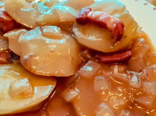 Slices of soft potato are covered in a rich brown sauce with onion and bacon.