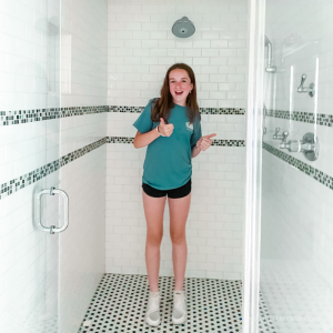 Marilee stands in the bathroom and gives a thumbs up